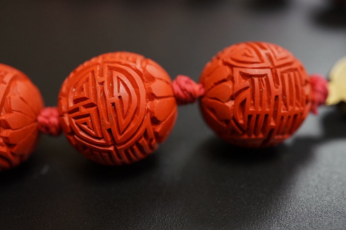 A Chinese red lacquered bead necklace and a bowenite jade figure of a cat